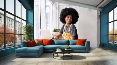 Happy stylish hipster African American teen girl with Afro hair using laptop computer in cafe, remote studying or working online, looking away enjoying sitting in cozy modern coffee shop table. Wall mural