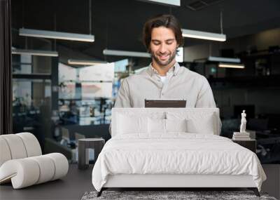 Happy young European business man executive holding pad computer at work. Male professional employee using digital tablet fintech device standing in office checking financial online market data. Wall mural