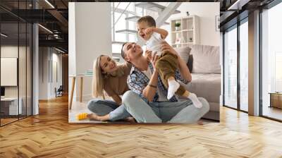 Happy young family couple having fun playing with cute small toddler kid son in modern living room together. Smiling parents mum and dad enjoying spending time with cute funny child boy at home. Wall mural