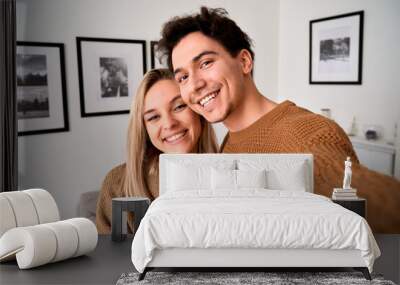 Happy young gen z couple hugging having fun looking at camera, holding phone taking selfie, shooting vlog or having virtual chat video call at home, close up headshot portrait, camera view. Wall mural