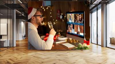 Happy young man wearing santa hat drinking champagne talking to friends on virtual video call meeting celebrate New Year party in holiday distance online conference chat together on computer at home. Wall mural