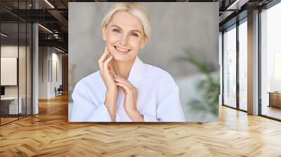 Headshot of happy smiling beautiful middle aged woman wearing bathrobe at spa salon hotel looking at camera touching face. Wellness spa procedures advertising. Skincare concept. Wall mural