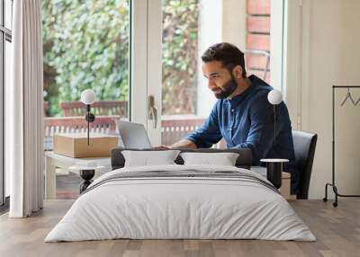 Indian ethnic business man, busy eastern male professional, serious businessman computing remote learning or distance working online typing on laptop using computer sitting at home office table. Wall mural