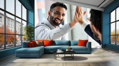 Indian happy smiling multiracial professional ceo businessman giving highfive to business partner after financial acquisition bank bargain contract at office. High five concept. Over shoulder view. Wall mural