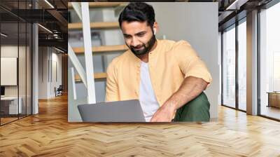 Indian man remote working on laptop device, using computer for virtual learning, surfing internet digital technology watching online web education webinar, having hybrid video call meeting from home. Wall mural