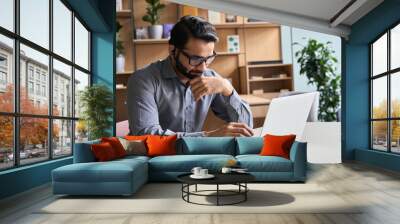 Latin indian serious businessman wearing glasses and headset having virtual team meeting call, remotely working at home watching online learning training webinar in remote office. Wall mural