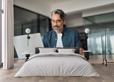 Mature busy businessman writing notes watching online webinar sitting at desk. Middle aged older professional business man using laptop working looking at computer technology in office. Wall mural