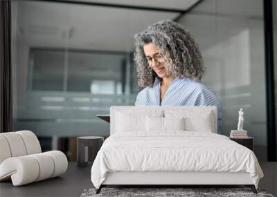 Mature busy happy businesswoman bank manager, older female corporate executive holding digital tablet standing at work. Middle aged professional business woman using tab computer in office. Wall mural