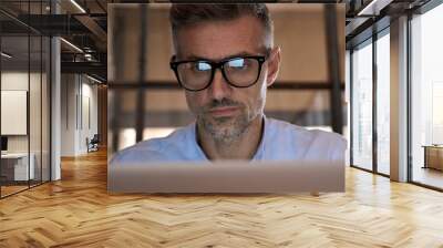 Mature concentrated business man trader wearing eyeglasses working looking at laptop computer screen reflecting in glasses analyzing online trading market financial digital data graph. Close up view Wall mural