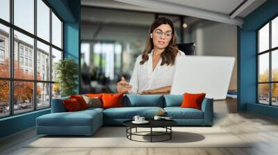 Mid aged business woman having hybrid meeting working in office. Busy mature female corporate leader executive, hr manager communicating by conference call, remote online job interview on laptop. Wall mural