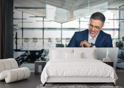 Middle aged smiling professional business man global company executive ceo manager or lawyer wearing suit sitting at desk in modern office working on laptop computer and writing notes, copy space. Wall mural