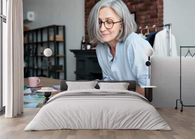 Middle aged stylish woman fashion designer drawing sketches in studio office. Mature old adult elegant grey-haired lady dressmaker small business owner creating new fashion design cloth in atelier. Wall mural