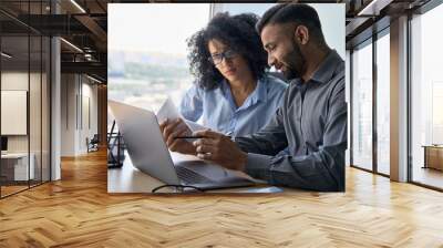 Multiethnic male indian mentor and female African American intern sitting at desk with laptop doing paperwork together discussing project financial report. Corporate business collaboration concept. Wall mural