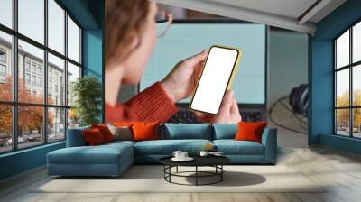 Over shoulder view of woman holding mobile phone with white blank mock up cellular screen applications working using cell phone. Cellphone display mock up for advertising apps concept. Wall mural