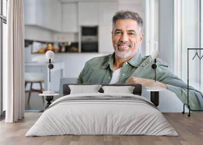 Portrait of happy smiling middle aged mature senior 50 years old bearded man wearing green shirt sitting on couch at home interior looking at camera relaxing on sofa in modern house. Wall mural