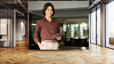 Portrait of young Hispanic professional business woman standing in office. Happy female company executive, smiling businesswoman entrepreneur corporate leader manager looking at camera using tablet. Wall mural