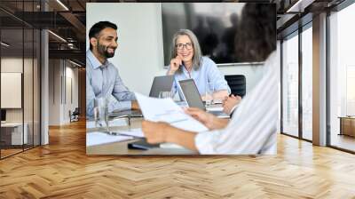 Senior female ceo and happy multicultural business people discussing company presentation at boardroom table. Smiling diverse corporate team working together in modern meeting room office. Wall mural