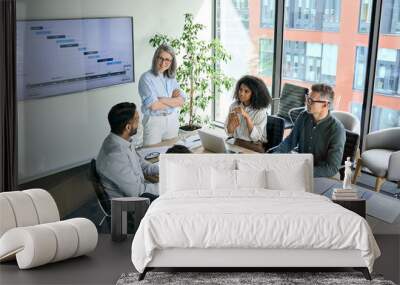 Senior female ceo and multicultural business people discussing company presentation at boardroom table. Diverse corporate team working together in modern meeting room office. Top view through glass Wall mural