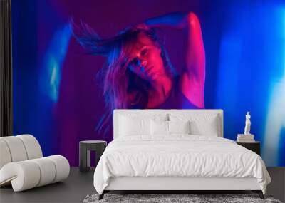 Sexy fashion attractive young adult girl model holding beautiful blond hair standing at purple studio background. Sensual pretty woman looking at camera alone in violet neon lights. Portrait. Wall mural