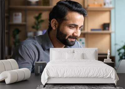 Smiling bearded indian businessman working on laptop at home office. Young indian student using computer remote studying, virtual training on video call meeting, watching online webinar or seminar. Wall mural