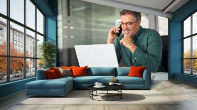 Smiling busy mature older professional business man executive manager talking on the phone making mobile call on cellphone in office working at laptop computer tech communicating at workplace. Wall mural