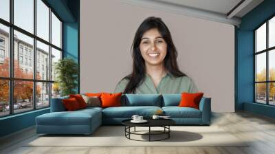 Smiling cheerful young adult indian woman looking at camera, happy pretty funny lady model laughing, feeling positive emotion standing isolated on brown background, face front headshot portrait. Wall mural