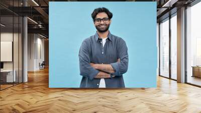 Smiling confident arab young man, male student, professional employee or programmer standing isolated on blue background. Happy handsome ethnic guy wearing shirt and glasses portrait. Wall mural