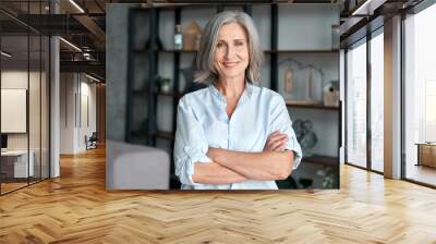 Smiling confident stylish mature middle aged woman standing at home office. Old senior businesswoman, 60s gray-haired lady executive business leader manager looking at camera arms crossed, portrait. Wall mural