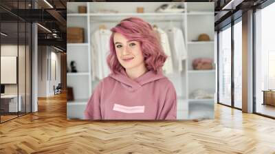 Smiling hipster gen z teen girl fashion designer, stylist with pink hair piercing wearing hoodie looking at camera in front of modern clothes wardrobe closet, face head shot close up portrait. Wall mural