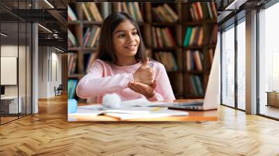 Smiling indian latin deaf disabled child school girl learning online class on laptop communicating with teacher by video conference call using sign language showing hand gesture during virtual lesson. Wall mural