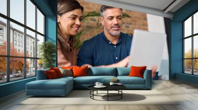 Smiling mature business man and woman having conversation looking at laptop, manager consulting client at meeting. Two happy professionals working using computer and talking sitting in office. Wall mural