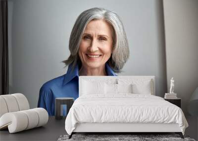 Smiling sophisticated mature grey-haired woman standing on grey wall background at home. Happy elegant middle aged old lady professional businesswoman entrepreneur posing in office, headshot portrait. Wall mural