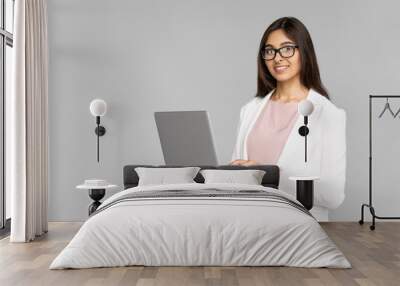 Smiling young adult indian businesswoman in white suit looking at camera. Happy woman holding modern computer in hands and standing isolated on grey background with copy space Wall mural