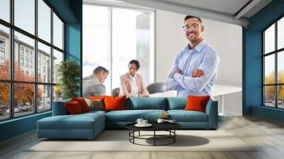 Smiling young confident Latin business man manager standing arms crossed at office team meeting. Portrait of happy professional businessman, male company employee leader in board room. Wall mural