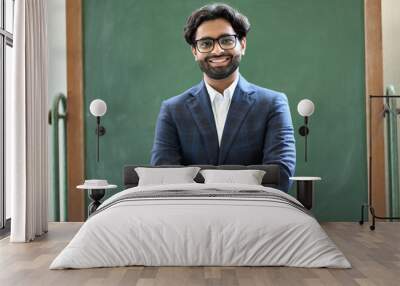 Smiling young indian business man professional manager wearing suit looking at camera standing arms crossed in office. Arab teacher or professor posing for portrait at work desk in front of blackboard Wall mural