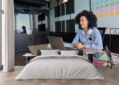 Successful African American businesswoman sitting at desk having working videoconference on yearly global financial report with client using laptop computer in contemporary corporation office. Wall mural