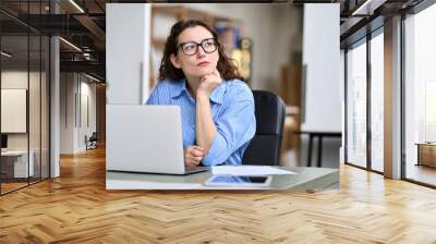 Thoughtful serious professional business woman employee or student using laptop, looking away thinking of question or idea, working or learning on computer feeling doubt, at home or in office. Wall mural