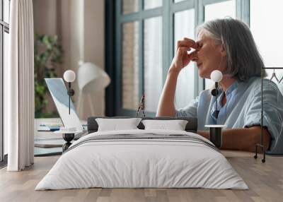 Tired old senior business woman taking off glasses suffers from eyestrain, stress, headache, fatigue after computer use work in office. Exhausted sick mature lady feels eye strain problem at workplace Wall mural