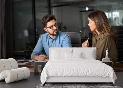 Two busy colleagues working together talking using tab device in office. Middle aged Latin female manager discussing work with young male worker discussing business plan strategy at office meeting. Wall mural