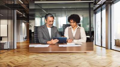 Two busy happy diverse professional business team people working in office using digital tablet. Older male executive manager talking to young female colleague having conversation sitting at work desk Wall mural