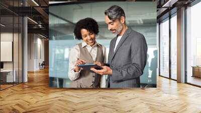 Two busy happy diverse professional business team people working in office with digital tablet. Male executive manager talking to female partners having conversation standing at work using tab. Wall mural