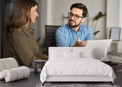 Two busy professional business people working in office with laptop computer. Mid aged mature Latin female executive manager talking to male colleague having conversation sitting at workplace. Wall mural