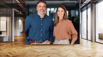 Two happy confident professional mature middle aged Latin business man and business woman corporate executive leaders company managers standing in office looking at camera, portrait. Wall mural