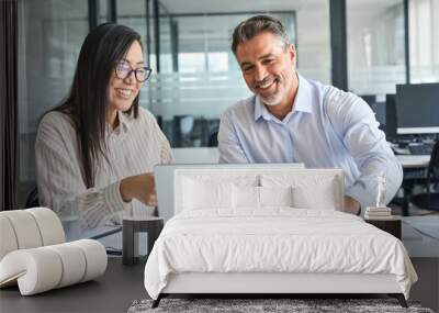 Two happy diverse professional colleagues Latin business man and Asian woman corporate executives working together in office using laptop, talking and looking at computer, having meeting discussion. Wall mural