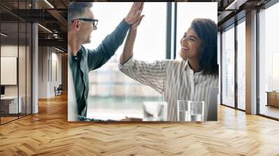 Two happy multiracial professional executive businessman and businesswoman colleagues giving highfive after victory of corporation project together at boardroom meeting. High five concept. Vertical. Wall mural