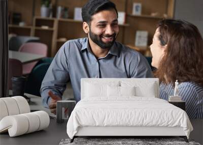 Two professionals - happy smiling indian hr manager and latin young female colleague at office meeting having fun. Mentoring Hispanic male teacher and female student in multiethnic creative space. Wall mural