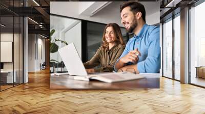 Two smiling professional business people talking using laptop computer working in office. Happy colleagues or entrepreneurs team man and woman discussing corporate technology at workplace. Wall mural