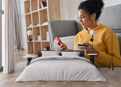 young adult african american female consumer holding credit card and smartphone sitting on floor at  Wall mural