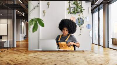 Young African American college student hipster woman with afro hair sitting at table in cafe indoor using laptop watching learning virtual online digital webinar. Wall mural