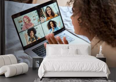 Young African American teen girl lying on bed having virtual meeting waving hand chatting with friends during online video call at home having fun using laptop computer. Over shoulder view Wall mural